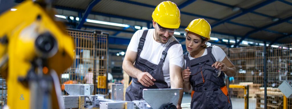 Deux personnes portant des équipements de protection consultent un ordinateur près d’un robot industriel.