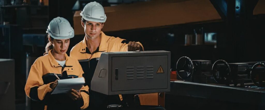 Deux professionnels en tenue de travail contrôlent une machine et consultent une tablette dans un atelier industriel.