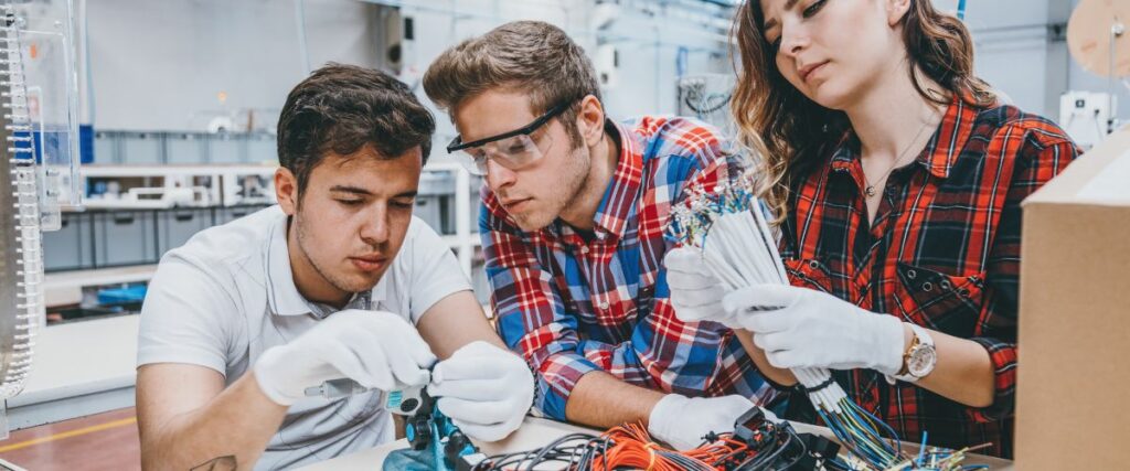 Trois personnes travaillent ensemble sur des composants et des câblages électroniques.